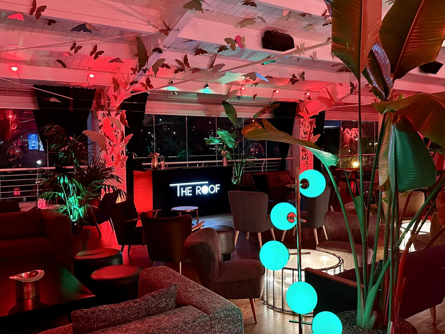 L'insegna al neon «The Roof» tra piante e una lampada a sfere verdi